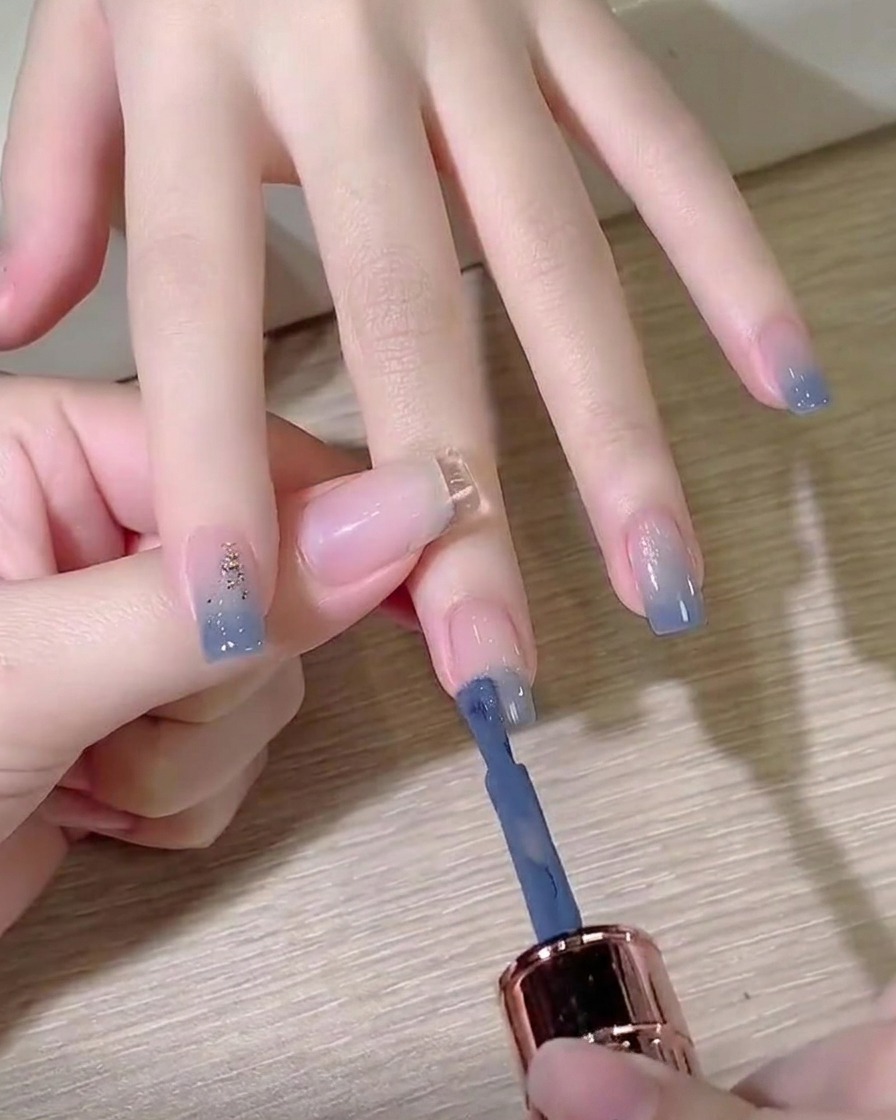 Il pennello di una boccetta di smalto gel che applica un colore blu polvere sulla punta di ununghia preparata.