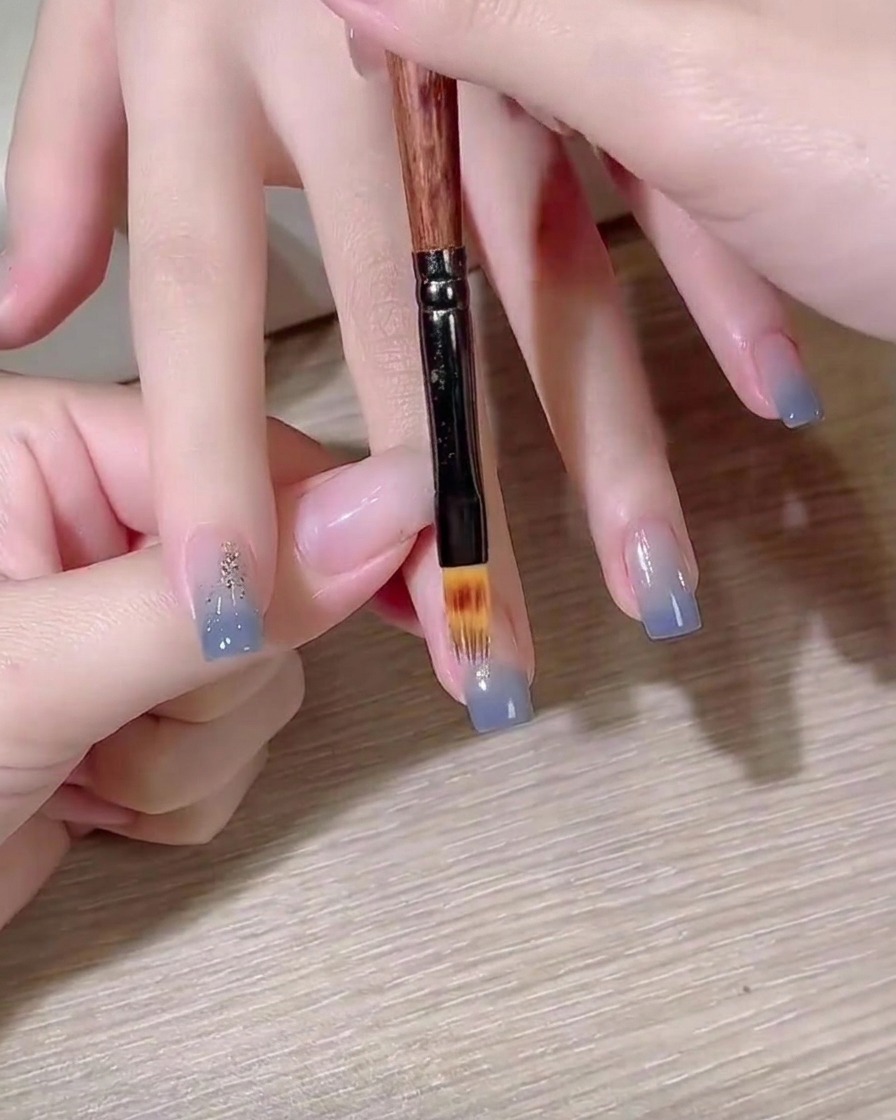 Un pennello piatto per gel che crea una sfumatura di colore blu su ununghia.