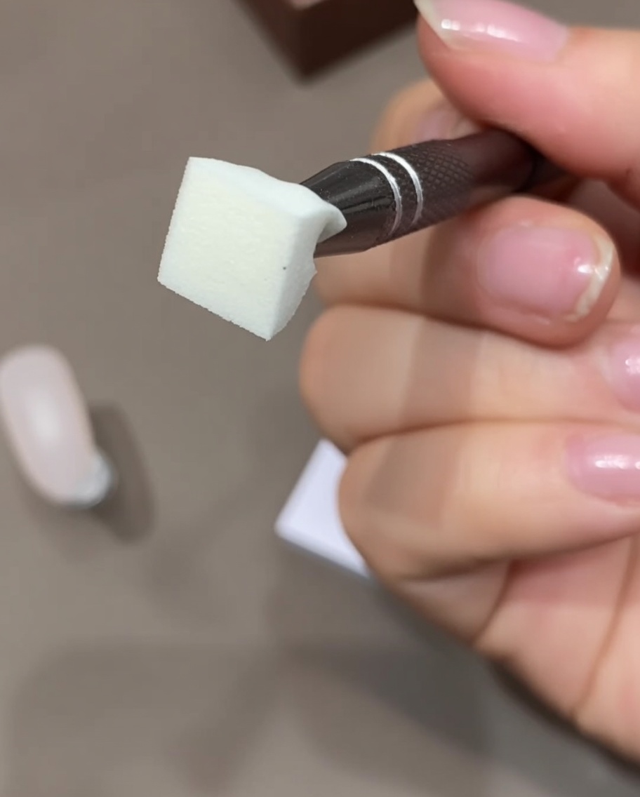 Primo piano di una mano che tiene una spugnetta per trucco usando del nastro adesivo per rimuovere la polvere in superficie.
