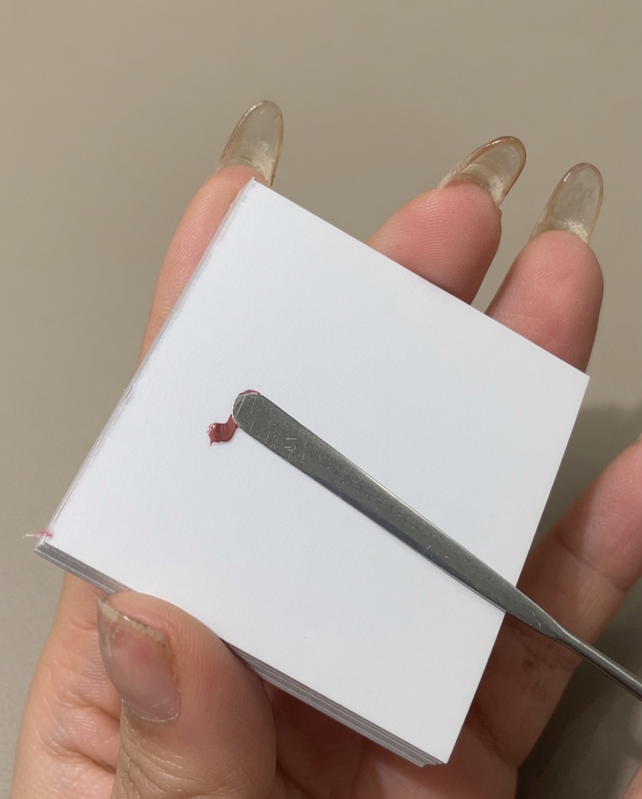 Una spatola in metallo che stende una linea di smalto gel colorato sulla superficie di una tavolozza.
