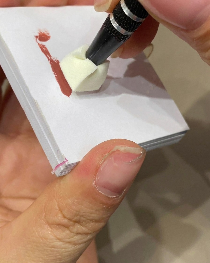 Una spugnetta da trucco che tampona il gel colorato sulla punta di ununghia con base nude per creare un effetto ombré.