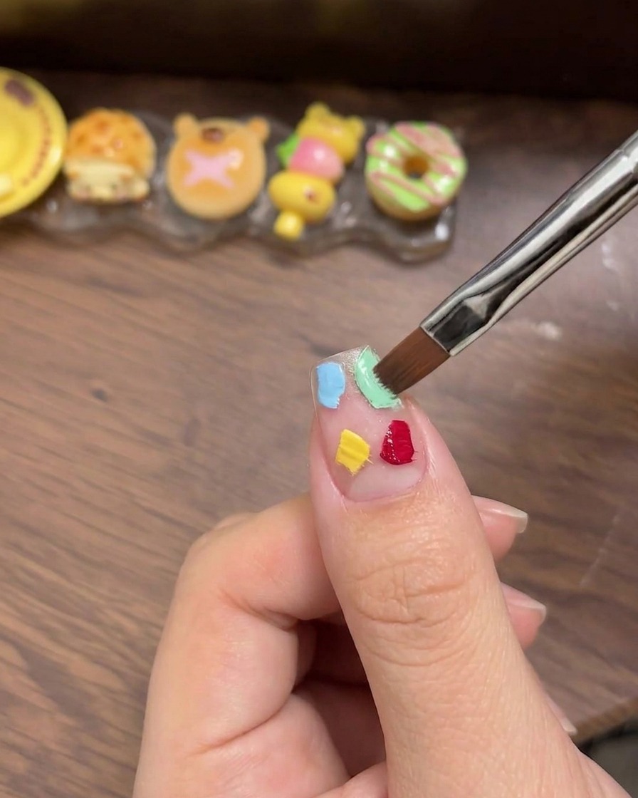 Una spugnetta cosmetica bianca utilizzata per tamponare e sfumare delicatamente quattro quadrati di gel colorato fino a ottenere un effetto ombré.