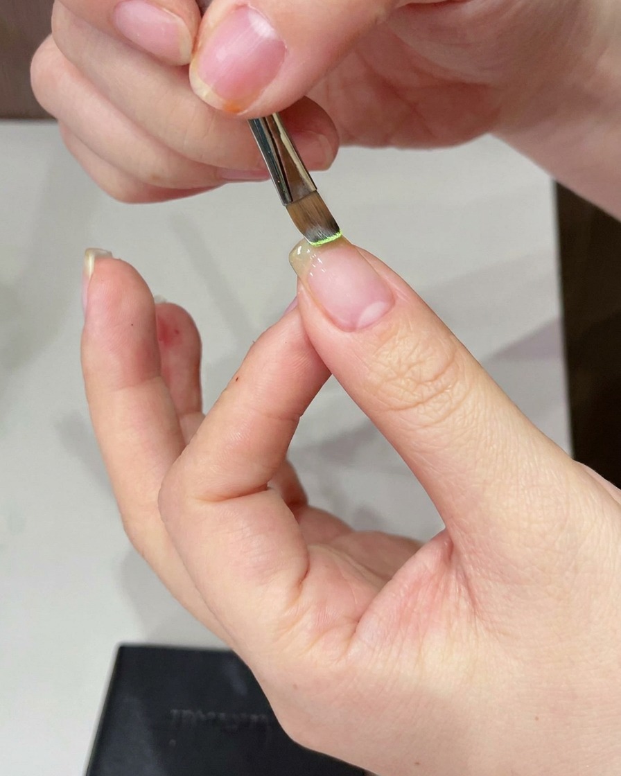 Dettaglio di un pennello che applica gel verde chiaro sulla punta dellunghia.