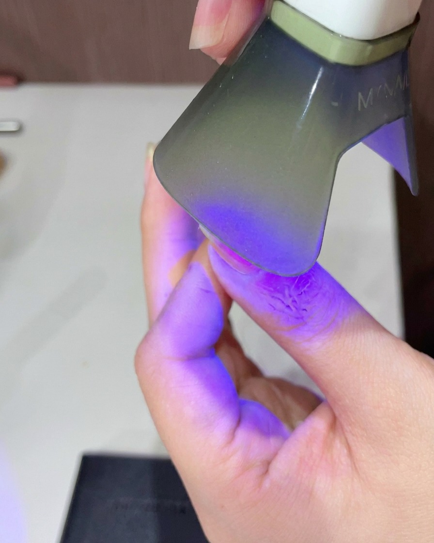 Primo piano di un dito posizionato sotto una piccola lampada UV LED portatile per polimerizzare il top coat rosa lucido.