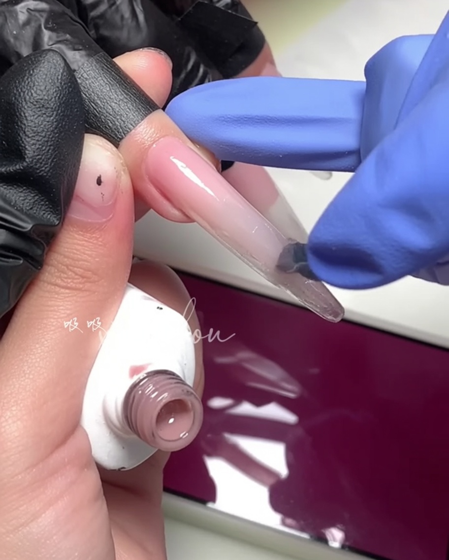 Un primo piano di un pennello che applica un gel magenta brillante sulla metà esterna dellunghia.