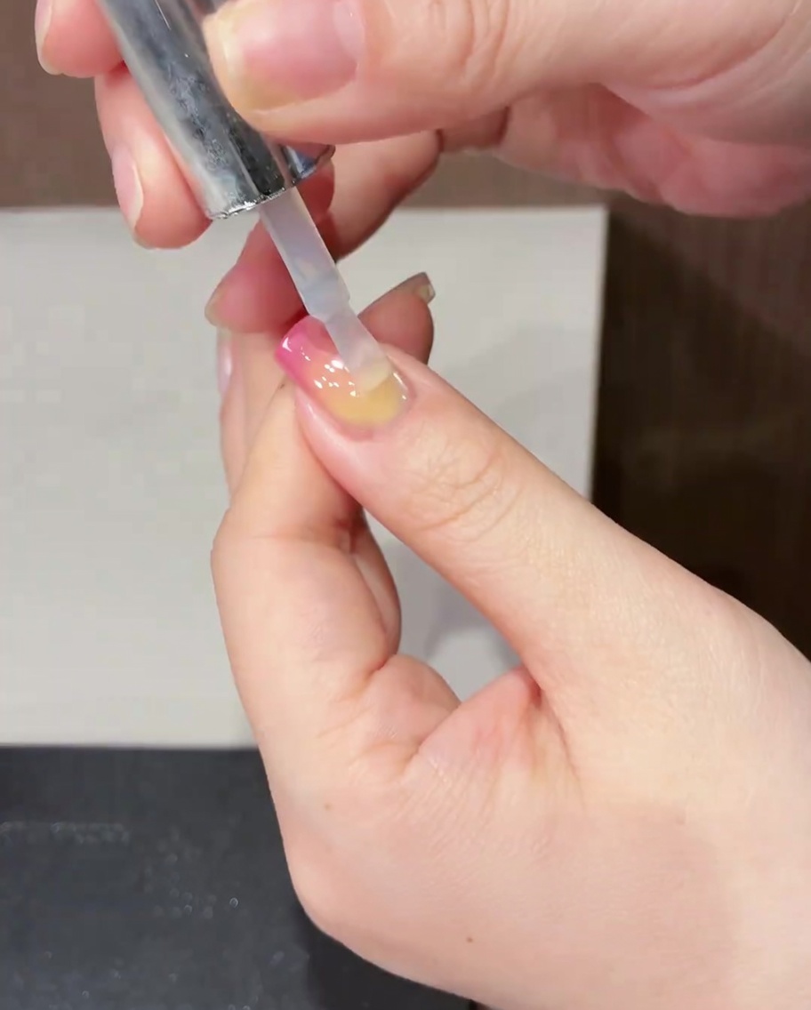 Un pennello che applica un top coat trasparente e lucido su un design completato per unghie a tulipano primaverile.