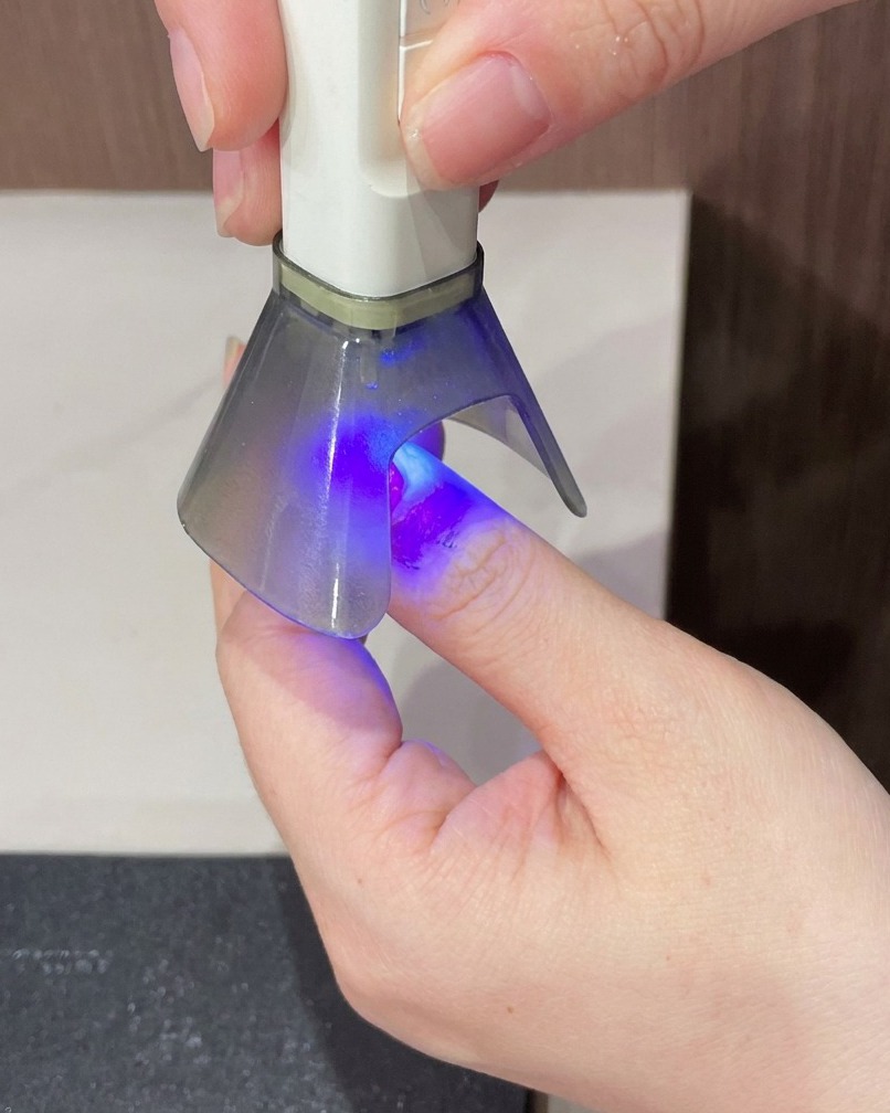Un dito tenuto sotto una lampada UV portatile per il passaggio di indurimento finale della manicure.