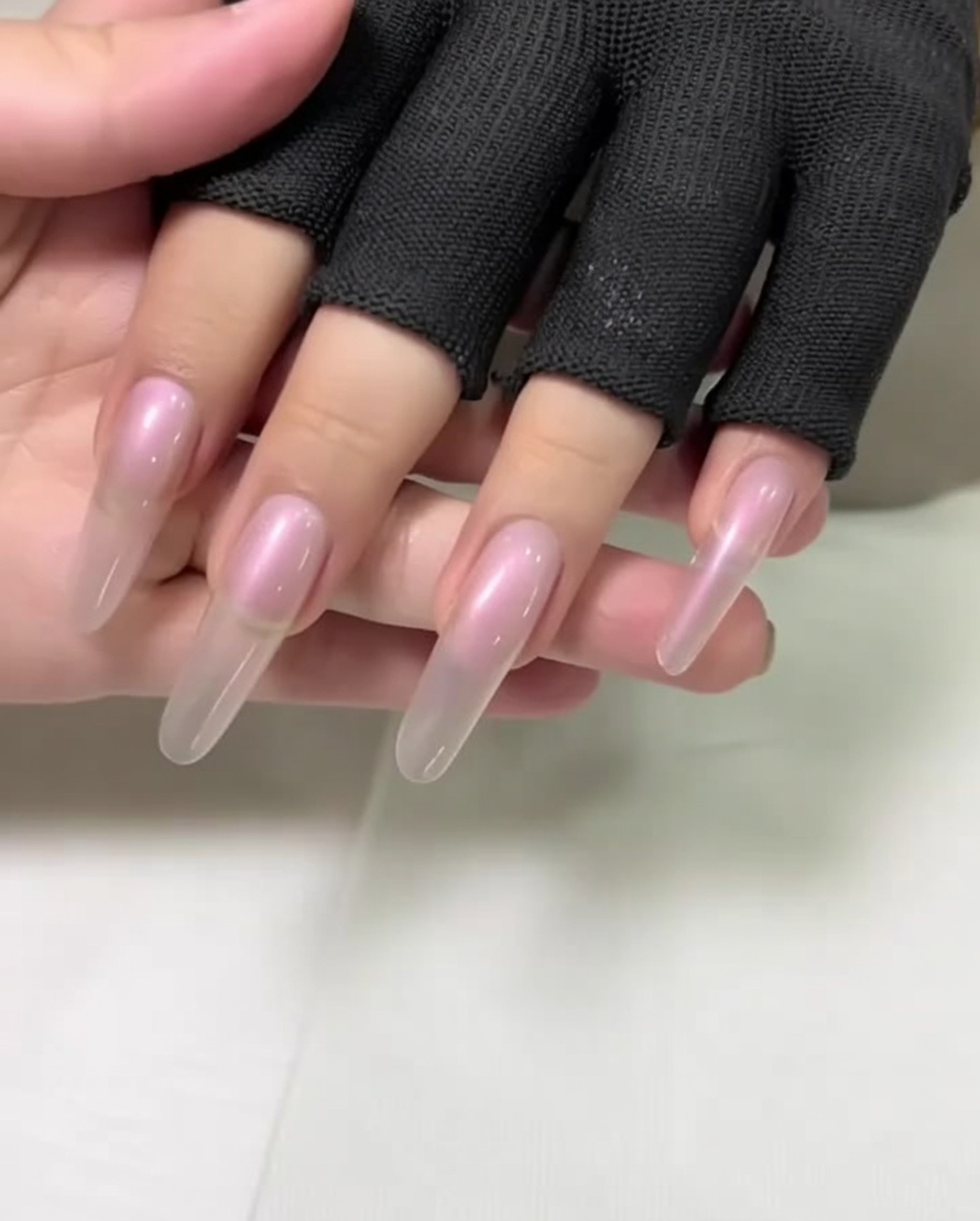 Primo piano di una mano con unghie lunghe a mandorla durante la spinta delle cuticole con uno spingicuticole in metallo.