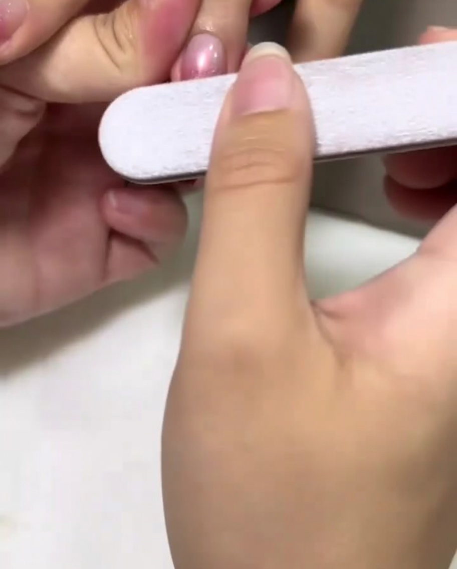 Una mano che tiene una lima per unghie mentre opacizza delicatamente il centro di ununghia color rosa.