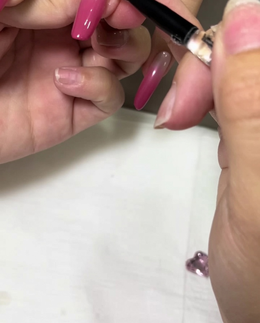 Un pennello di precisione che applica una goccia di gel adesivo trasparente su ununghia ombré rosa.