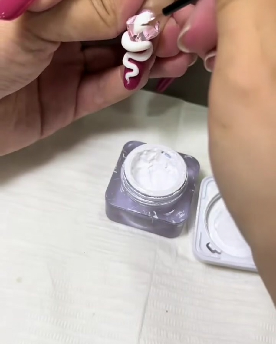 Un pennello sottile che applica gel bianco per aggiungere texture al design di un serpente 3D su ununghia.