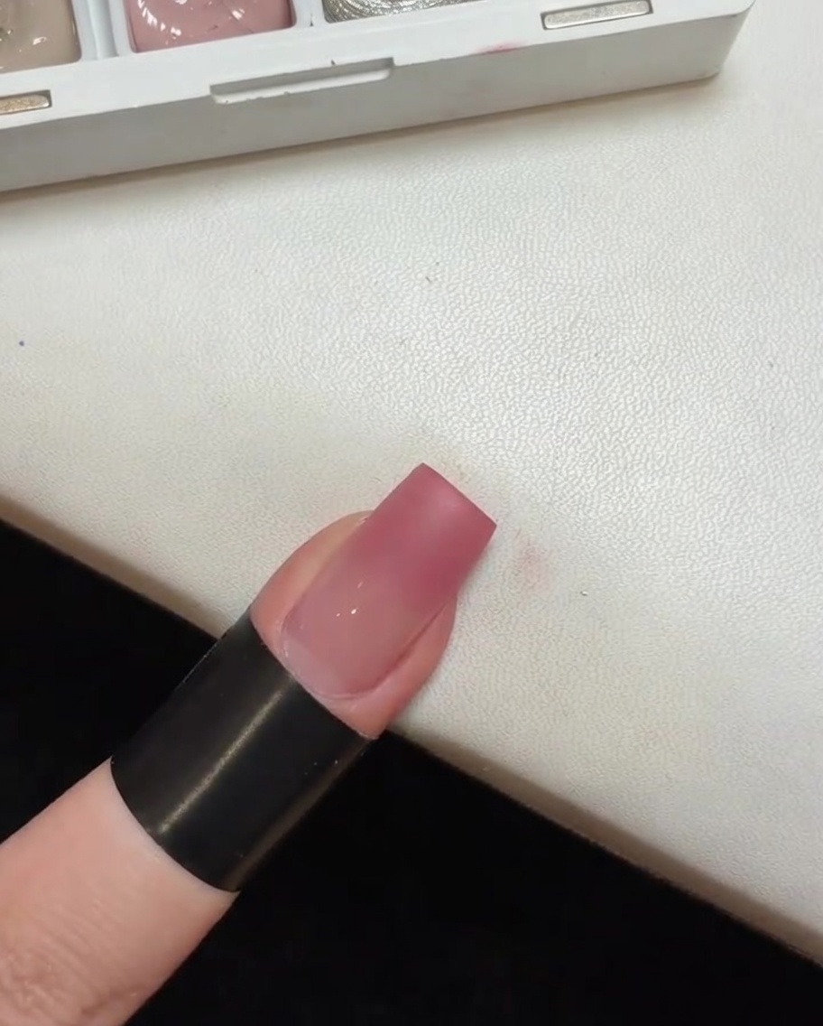 Ununghia con una base sfumata rosa che polimerizza allinterno di una piccola lampada UV portatile.