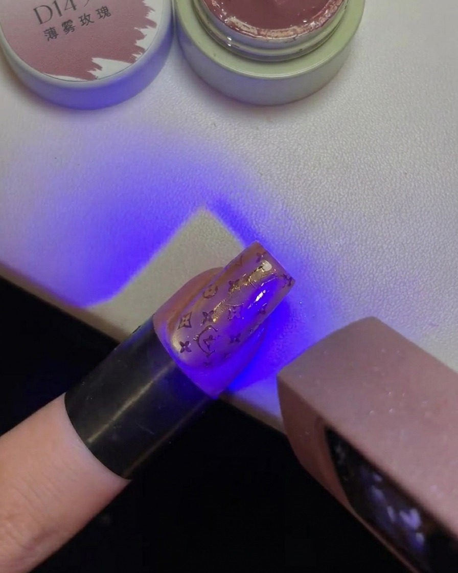Un dito con un design di Hello Kitty stampato sullunghia, tenuto sotto la luce viola di una lampada UV.