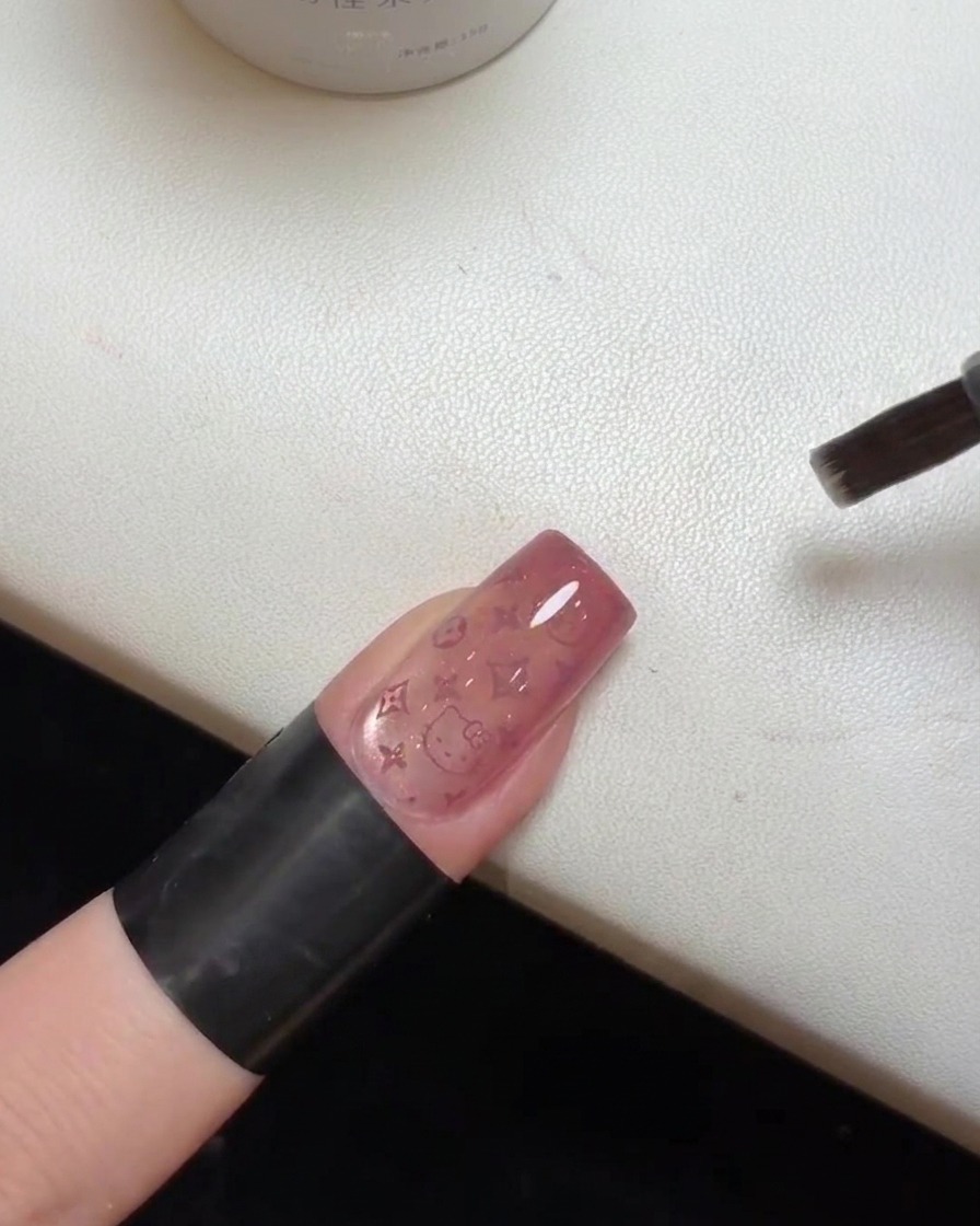 Primo piano di ununghia finita con il top coat in fase di polimerizzazione sotto una lampada UV.