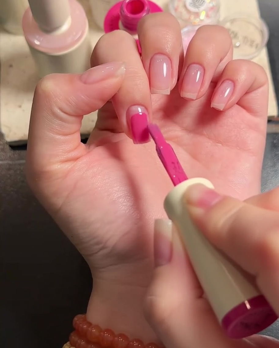 Primo piano di un pennello piatto che stende lo smalto gel rosa sulla superficie dellunghia.