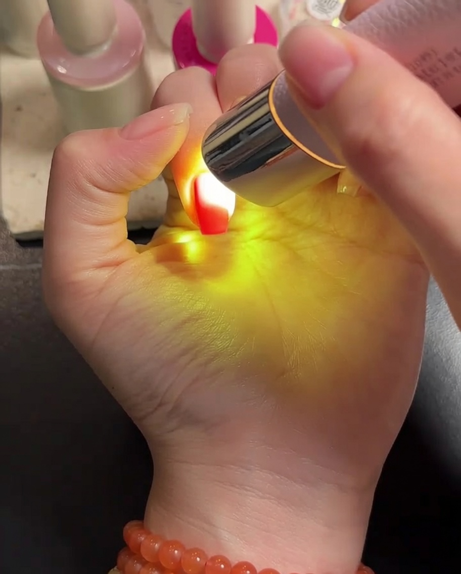 Una mano posizionata sotto una lampada LED portatile, con le unghie ricoperte di gel in fase di asciugatura.