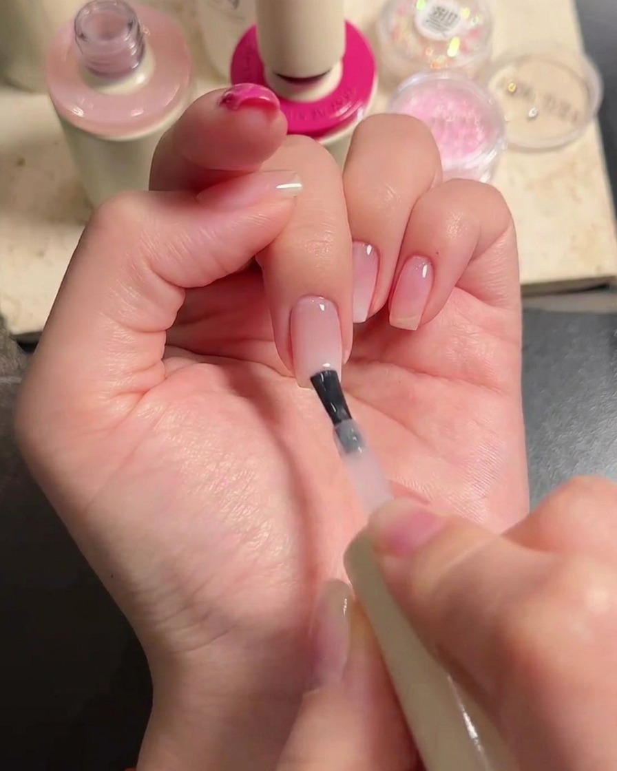 Un pennello applica uno strato di smalto gel nude traslucido sul medio e sullanulare per sfumare il design.