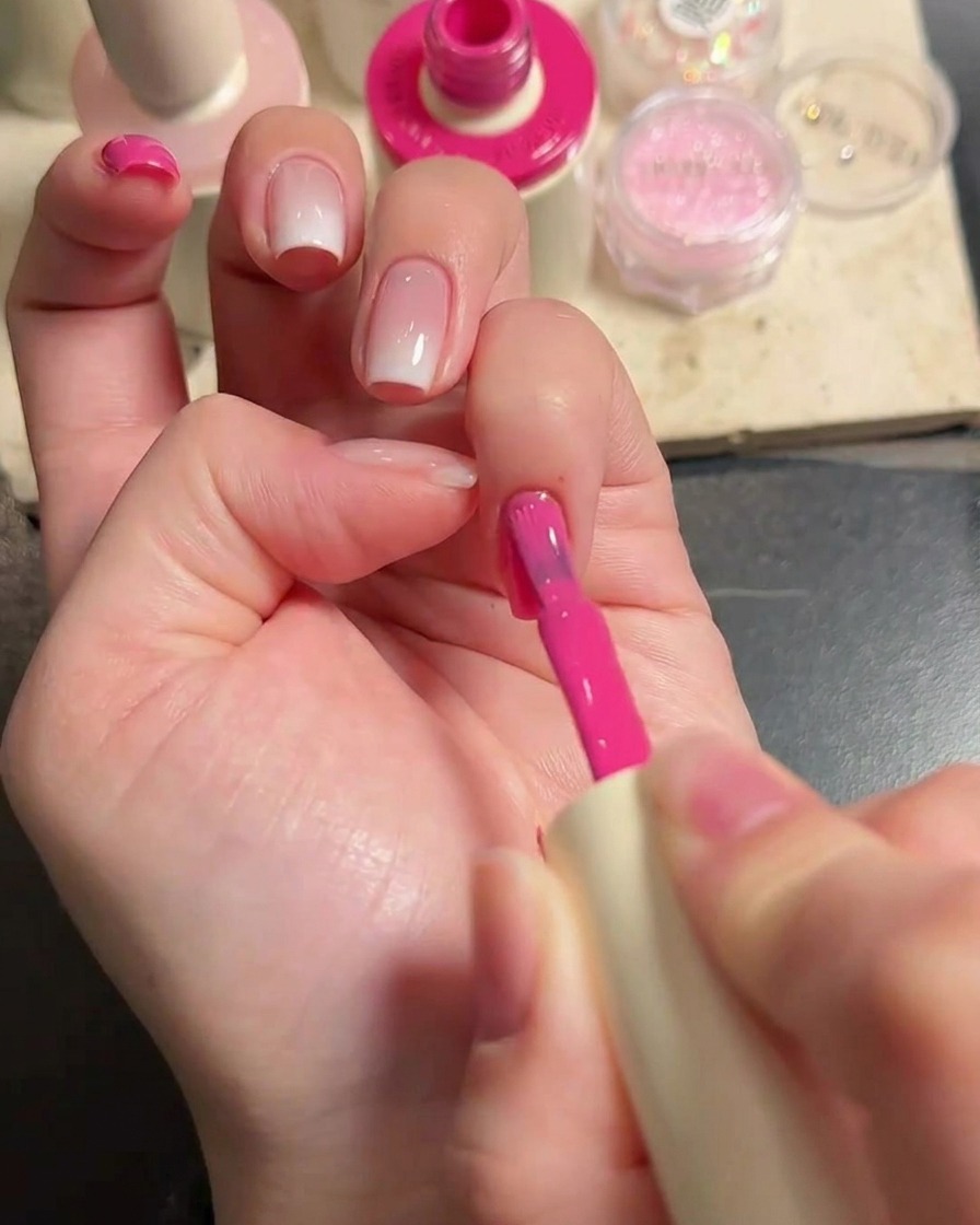 Primo piano di una mano con un pennello che applica uno smalto gel rosa vibrante sulle unghie.