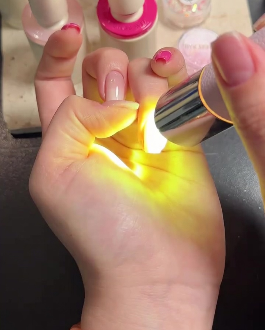 Una mano posizionata sotto una lampada LED con le dita chiaramente visibili durante la polimerizzazione del top coat.