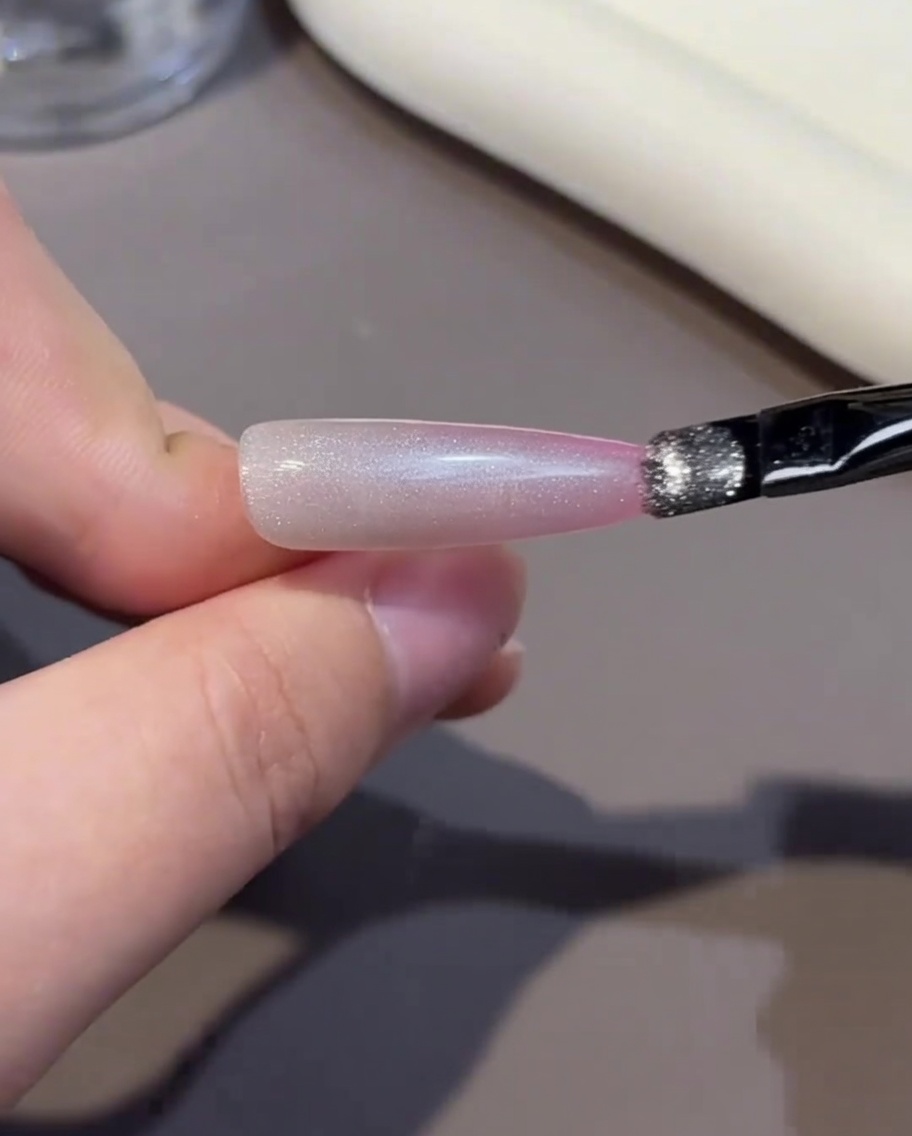 Un pennello applica uno strato di smalto gel rosa sulla punta dellunghia.