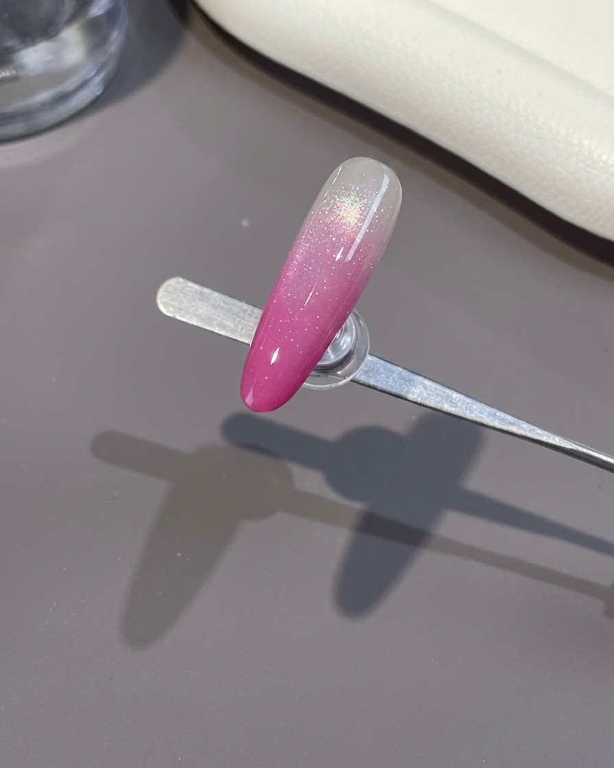 Un pennello applica un top coat trasparente e brillante su ununghia ombré rosa terminata.