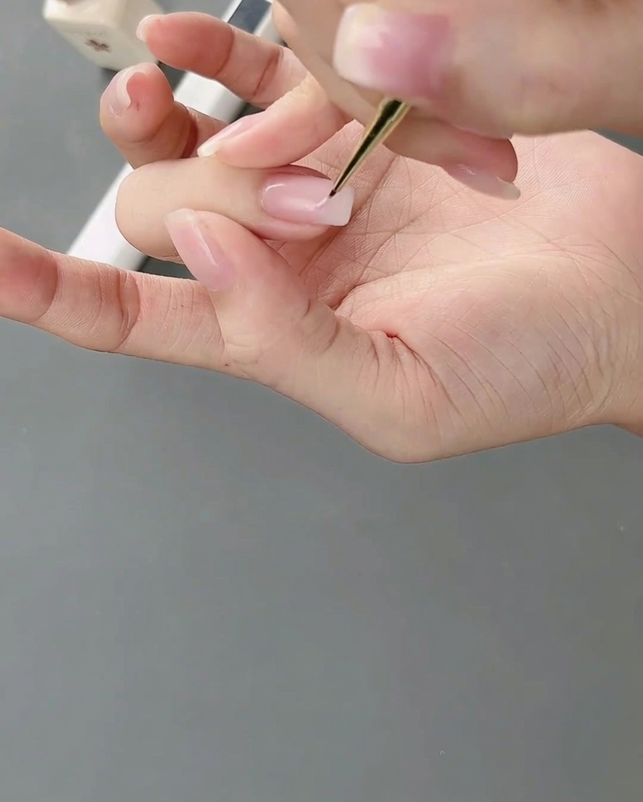 Un pennello da nail art a punta fine applica del gel rosa chiaro su ununghia per formare blocchi di colore irregolari.