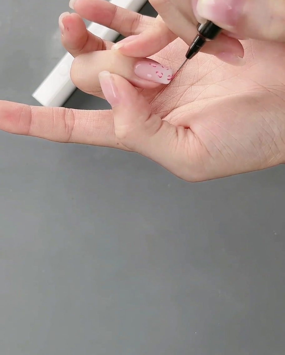 Una mano posizionata sotto una lampada per unghie polimerizza la nail art con linee sottili appena dipinte.