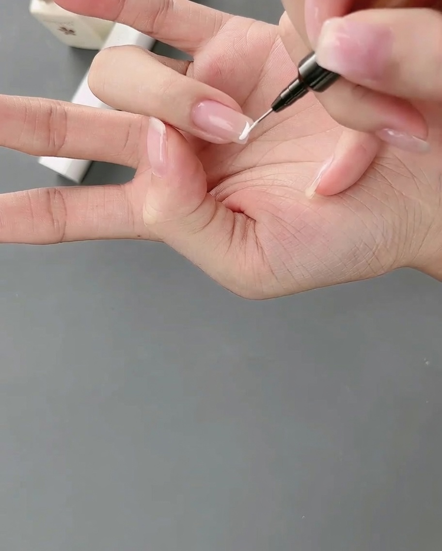 Un pennello liner applica una linea precisa di gel bianco per creare una french alta su ununghia.