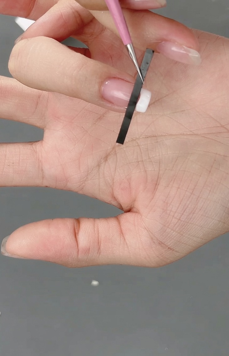 Primo piano di un adesivo per unghie french posizionato sulla punta dellunghia per creare una guida a griglia.