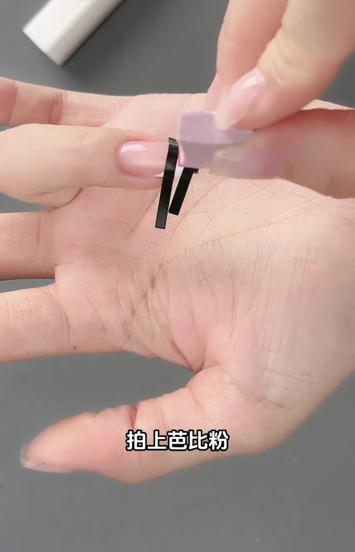 Un piccolo strumento a spugna tampona dello smalto gel rosa chiaro sopra la griglia creata dalladesivo french su ununghia.