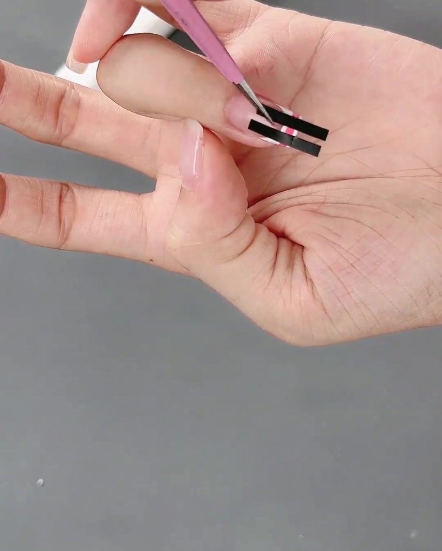 Pinzette rimuovono delicatamente il nastro adesivo da ununghia per rivelare un motivo a scacchi rosa e bianco.