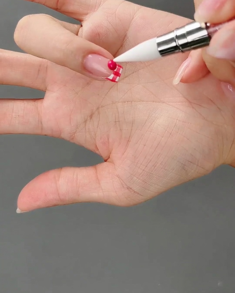 Uno strumento in silicone punta a una piccola perla rotonda di gel rosa scuro appoggiata su una punta french a scacchi.