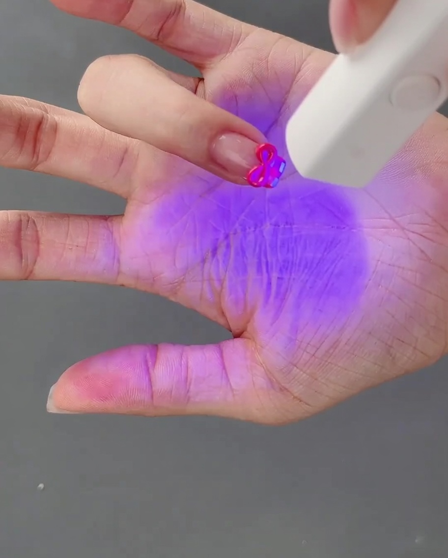 Una mano con un fiocco in gel 3D appena modellato viene polimerizzata sotto una lampada per unghie UV.