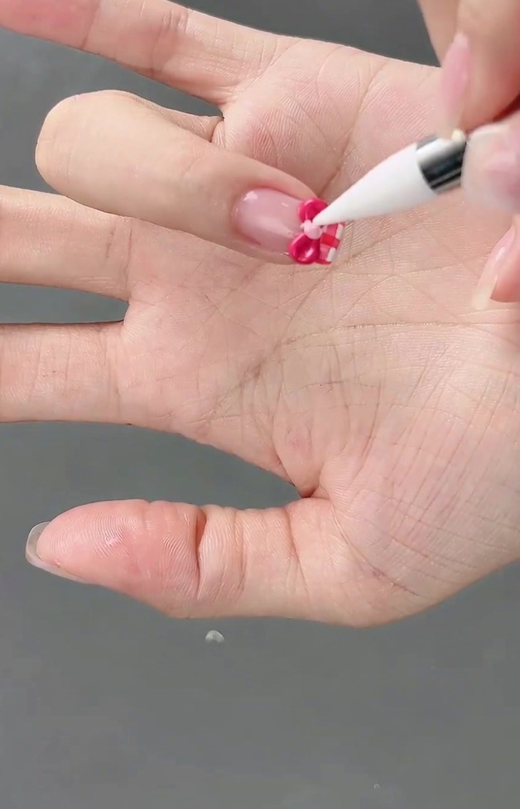 Una piccola perla di gel rosa chiaro viene posizionata al centro di un fiocco 3D utilizzando un pennello per dettagli.