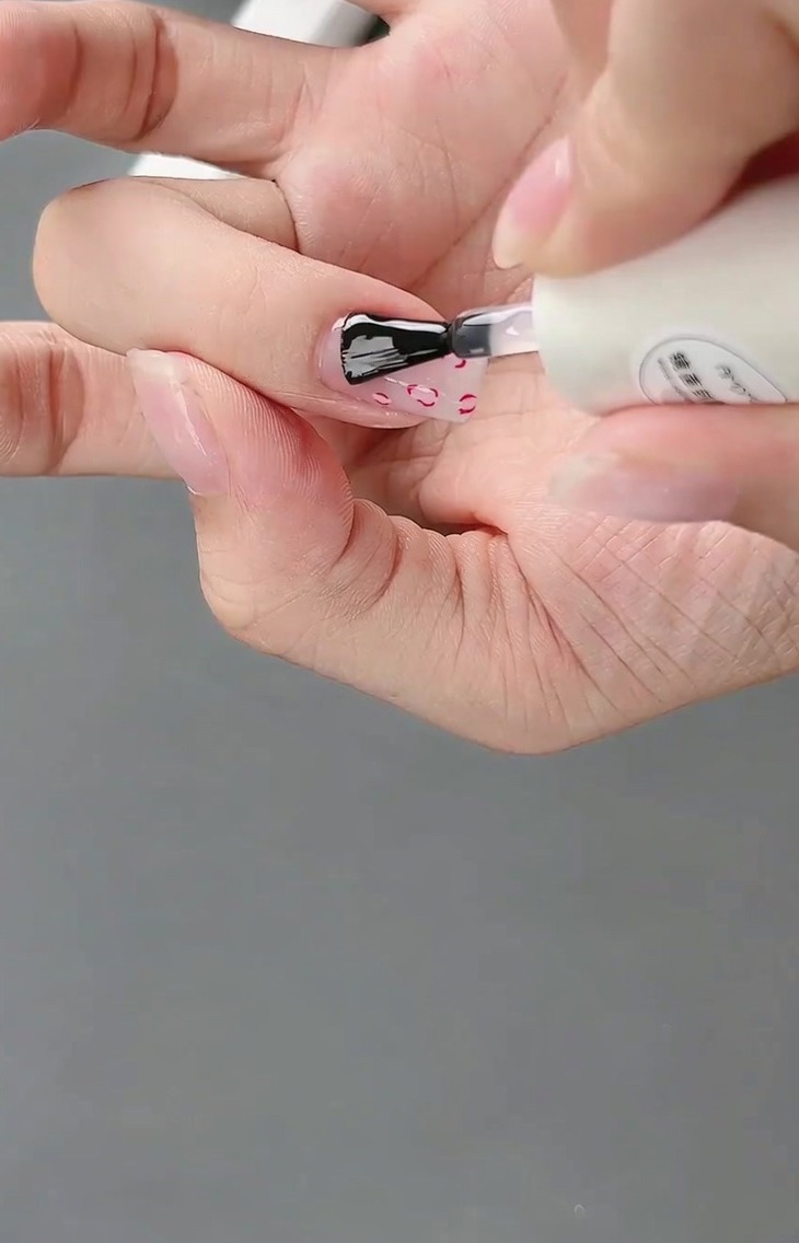 Un pennello applica un top coat finale lucido sul design completato con french e fiocco 3D.