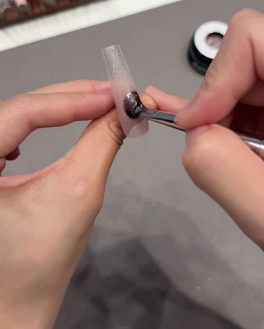 Un pennello che applica uno smalto gel cat eye scintillante sullintera superficie della tip.