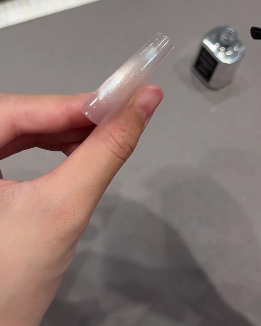 Un pennello nero che applica il top coat trasparente su unestensione per unghie con gel cat eye scintillante.