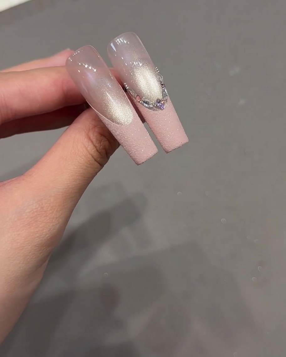 Primo piano di ununghia con un intricato design French caratterizzato da una varietà di strass allineati lungo la punta.