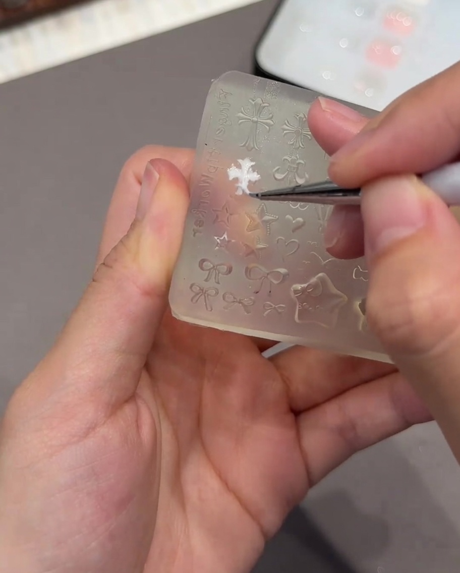 Un paio di pinzette che tengono un piccolo stampo 3D a forma di cuore bianco, preparandosi a posizionarlo su ununghia.