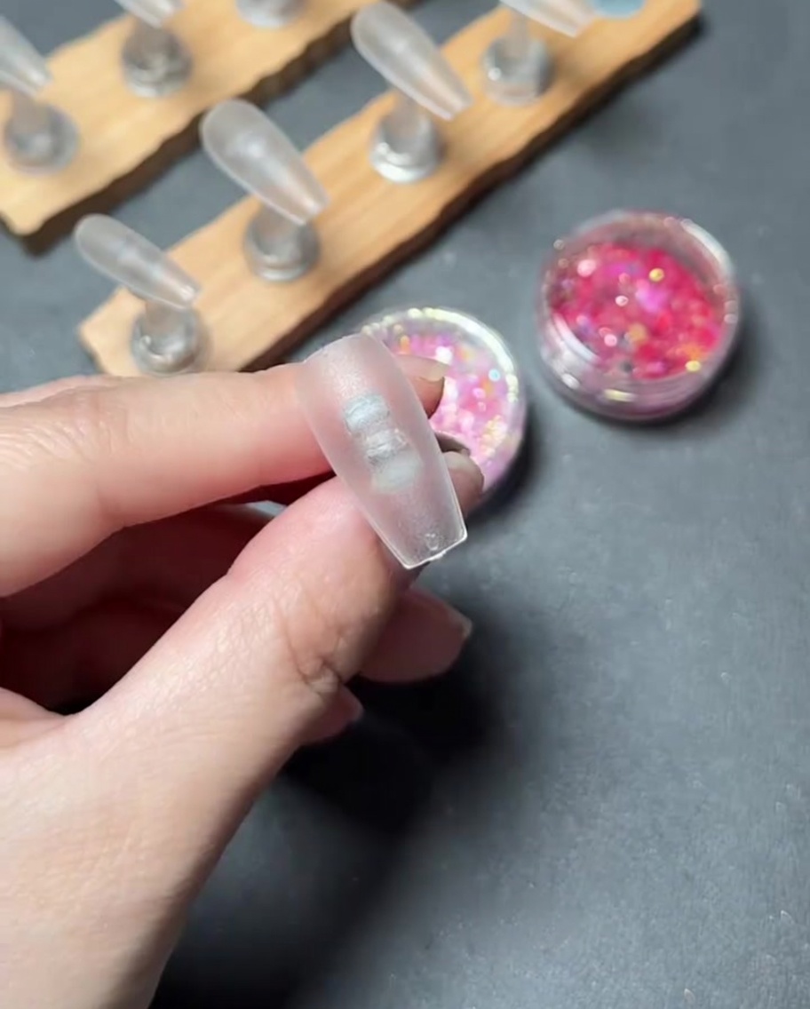 Un primo piano di un pennello che applica il gel base trasparente sulla superficie di una tip per unghie trasparente.