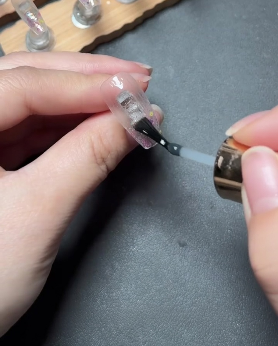 Applicazione di un gel rinforzante trasparente e denso sulla punta dellunghia coperta di glitter.