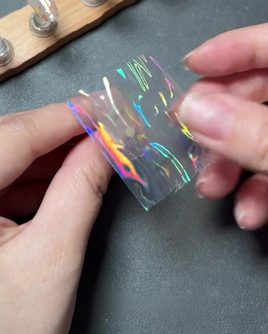 Dita che posizionano con cura un piccolo pezzo di pellicola transfer olografica sul centro di ununghia.