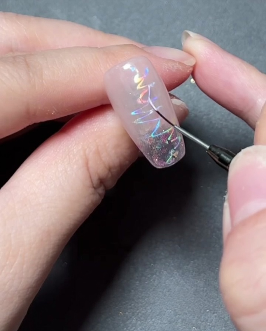Un pennello a punta sottile che dipinge una delicata forma a stella con gel colorato su ununghia sventagliata olografica.