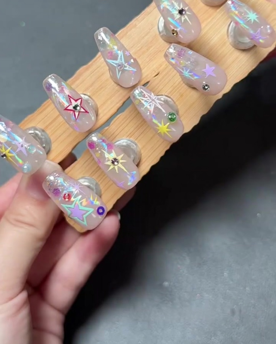 Un primo piano di una mano che posiziona un piccolo strass su ununghia decorata usando uno strumento.