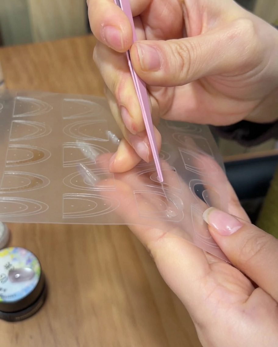 Delle pinzette posizionano un adesivo guida per French manicure sulla punta di ununghia curata.