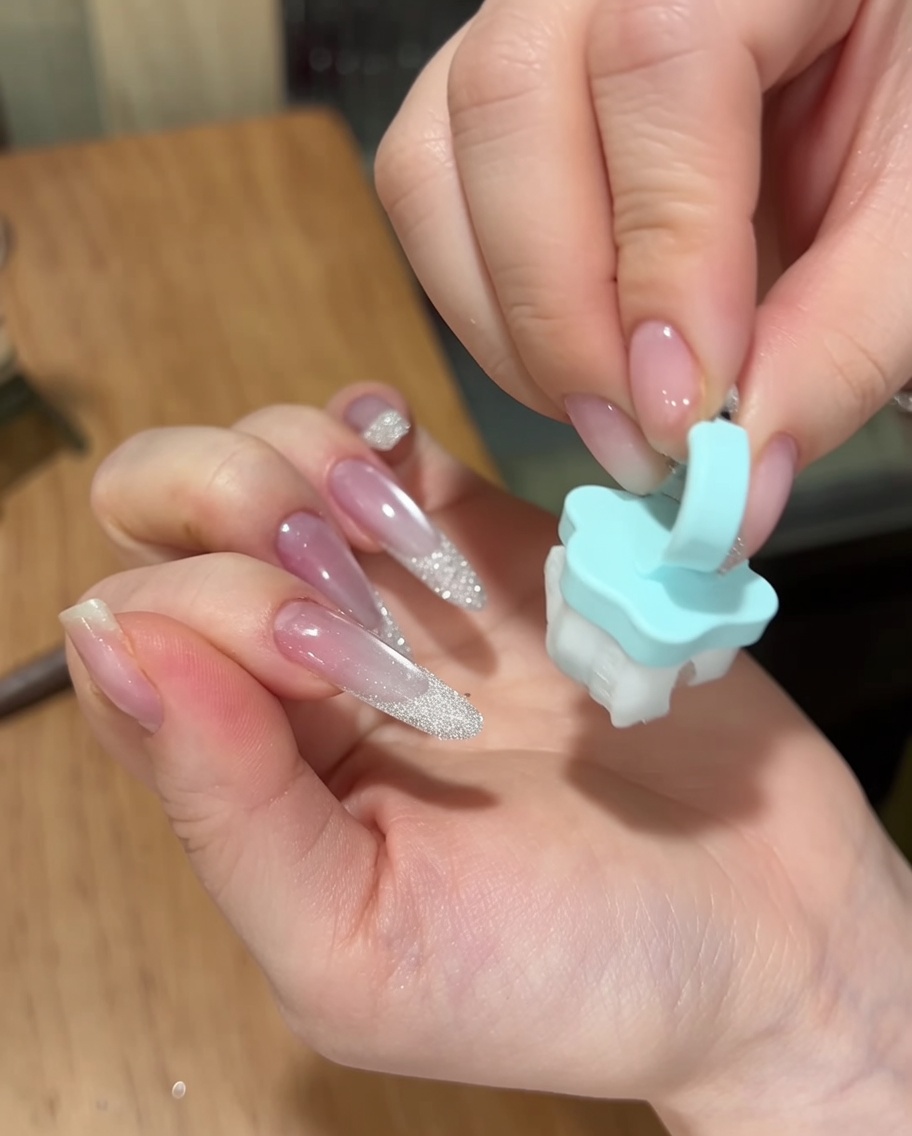 Una mano usa un piccolo pennello morbido blu per spolverare la polvere di zucchero in eccesso dalla superficie di una manicure finita.