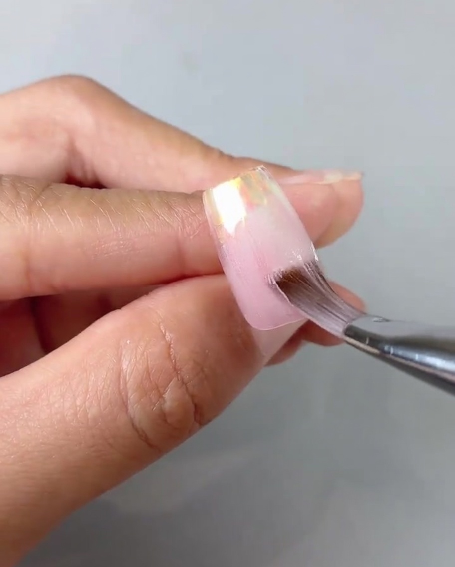 Primo piano di un pennello che uniforma e sfuma il gel rosa sheer su una tip.