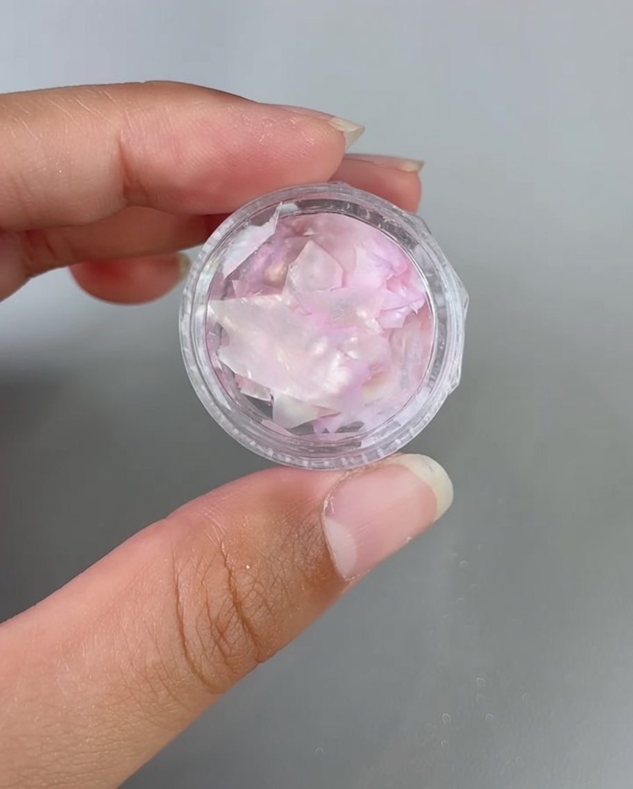 Pinzette che posizionano frammenti di conchiglia iridescente su ununghia rivestita di gel.
