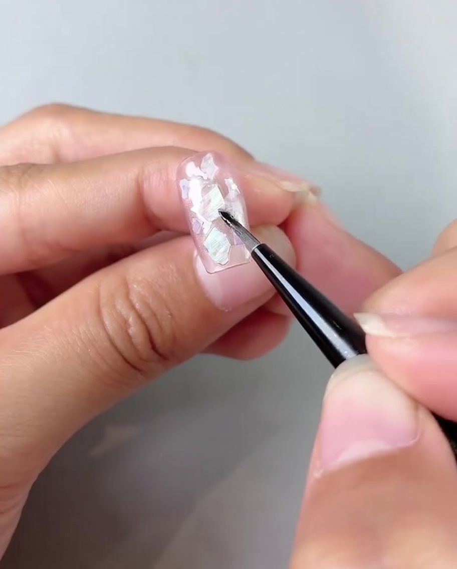 Un pennello che sfuma il gel bianco lattiginoso negli angoli di ununghia rosa cat-eye.