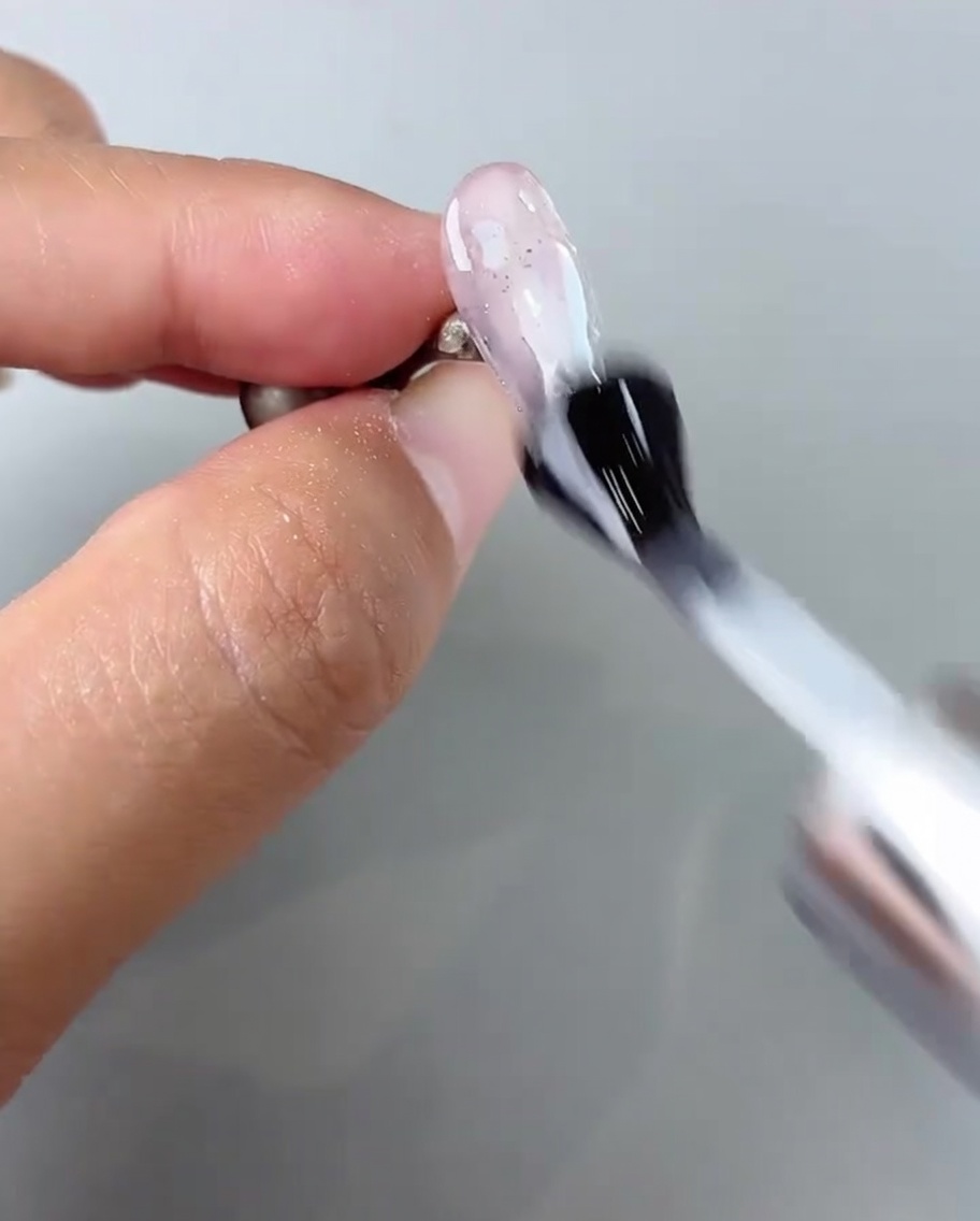 Un pennello applica un top coat lucido sopra la nail art completata.